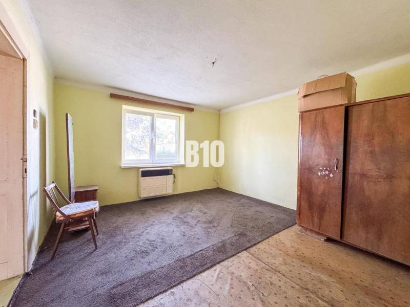 Jednoduchý pokoj v rodinném domě s kobercem a dřevěným nábytkem.