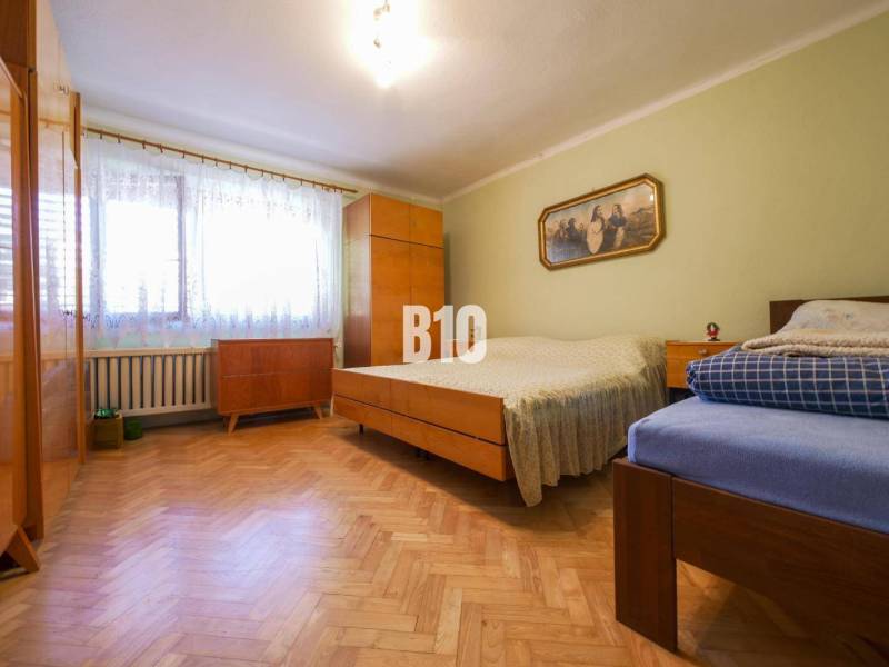 Ložnice s dřevěnou podlahou a jednoduchým nábytkem v rodinném domě.