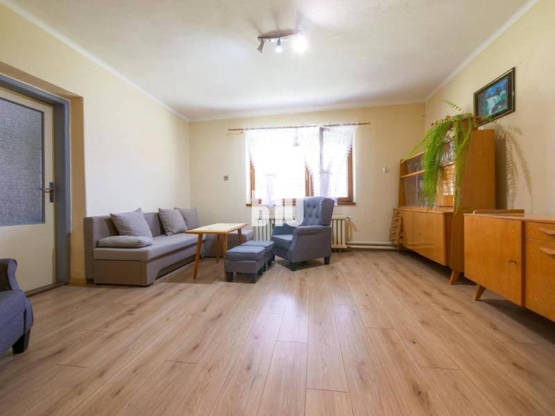 Obývací pokoj v rodinném domě s dřevěným nábytkem, šedou pohovkou a světlou podlahovou krytinou.