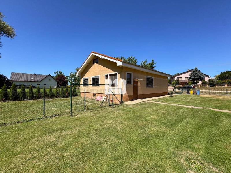 Rodinný dům v Nových Sadech obklopený prostornou, zelenou zahradou a plotem.