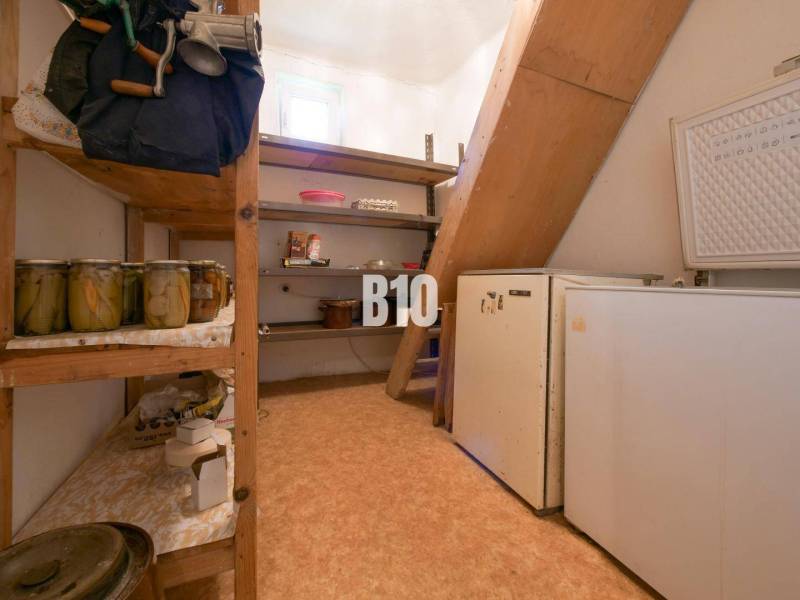 Spíž v rodinném domě s policemi, konzervami a starší ledničkou.