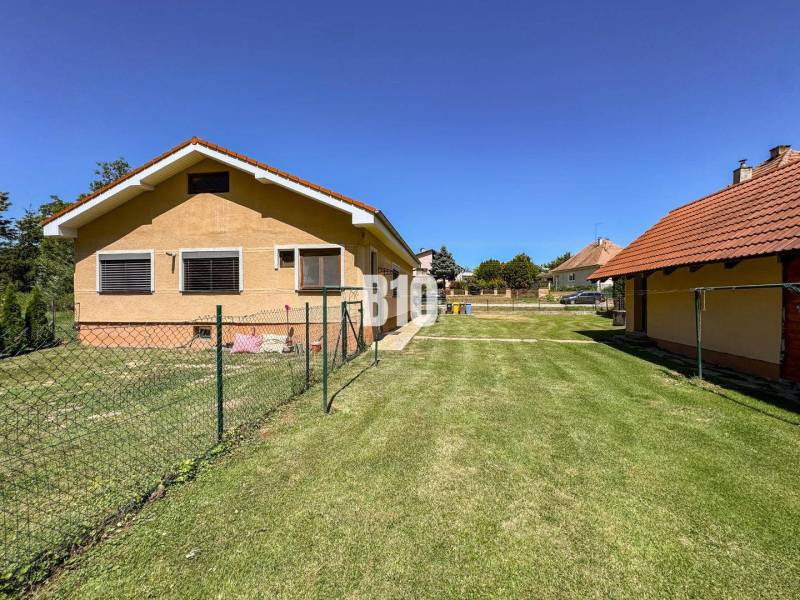 Rodinný dům v Nových Sadech se dvěma budovami a travnatým pozemkem, obklopený plotem.