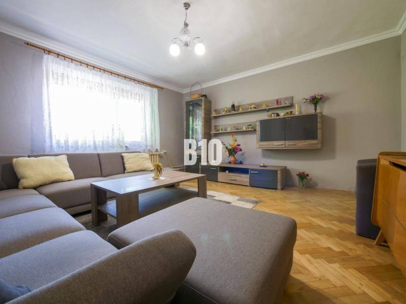 Obývací pokoj s rohovou sedačkou, dřevěné parkety, dekorativní police a osvětlení v rodinném domě.