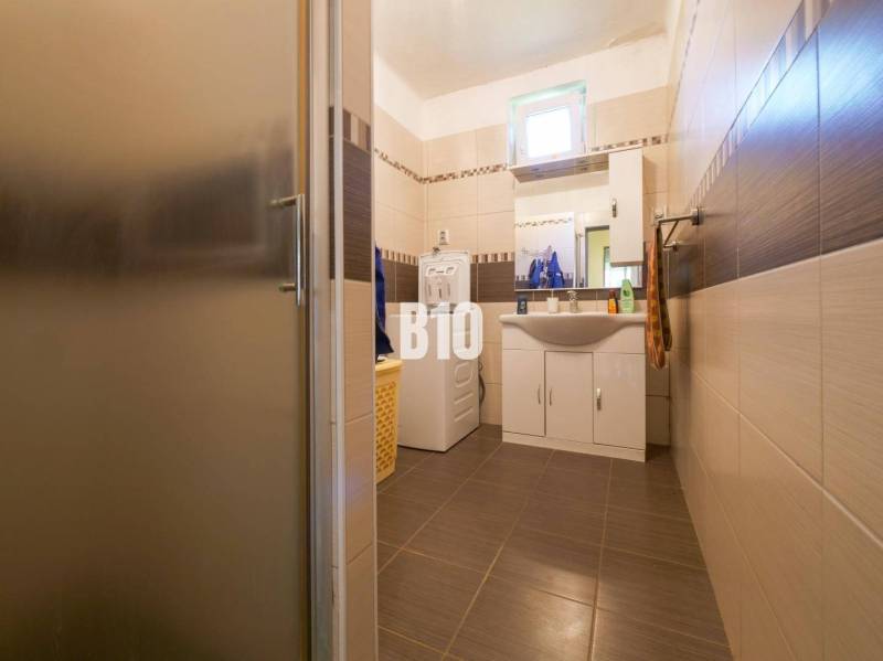 Koupelna v rodinném domě s pračkou a umyvadlem, obložená hnědými dlaždicemi.