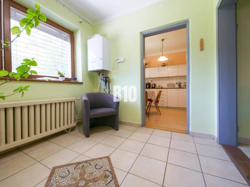 Interiér rodinného domu s předsíní, rostlinou, křeslem a výhledem do kuchyně.