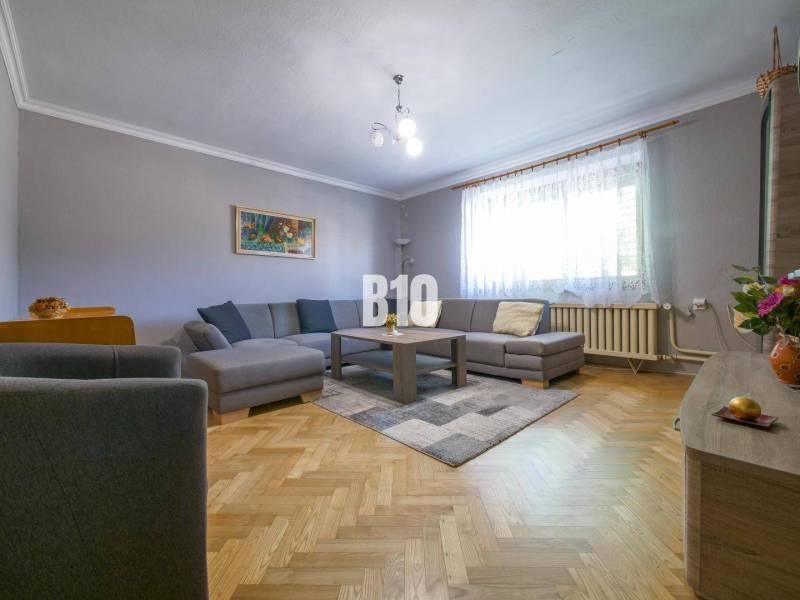 Obývací pokoj v rodinném domě s hnědou podlahou, šedou sedačkou a velkým oknem.