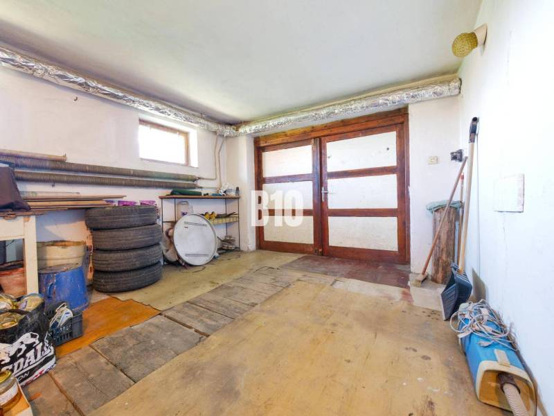 Garáž v rodinném domě s dřevěnými dveřmi a podlahou podobnou dřevěnému dekoru.