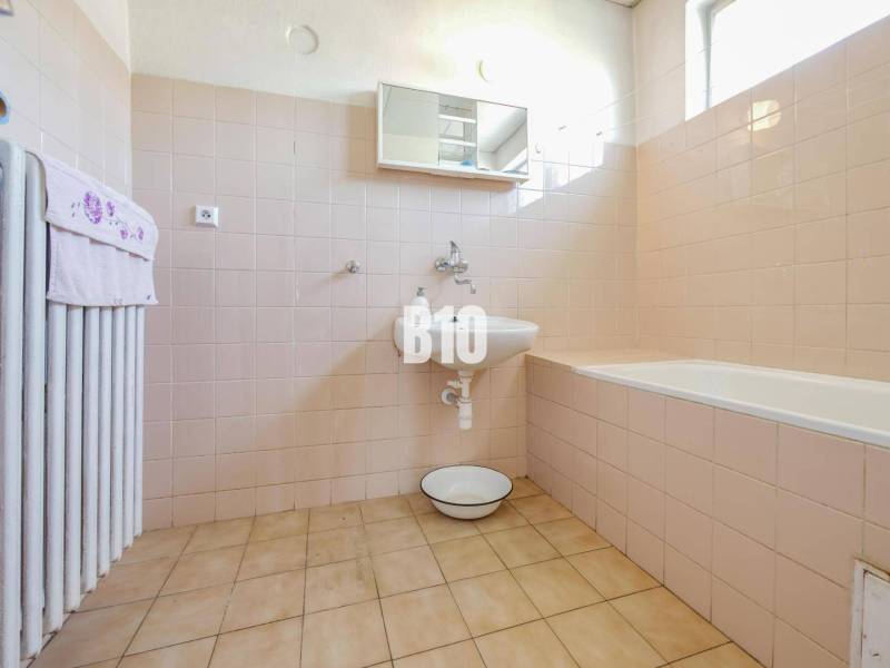 Koupelna v rodinném domě s vanou a světlými obklady na stěnách.