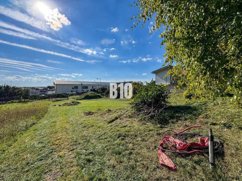 Pozemek na bydlení v Nitře, travnatá plocha se zelení a slunečnou oblohou.