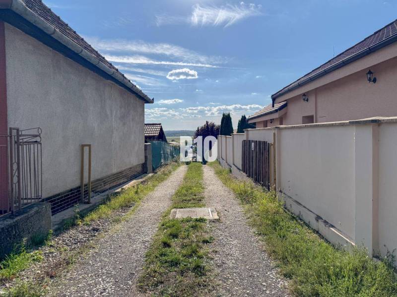 Úzká cesta mezi domy v lokalitě Pozemky - bydlení, Nitra, vedoucí k panoramatu krajiny.