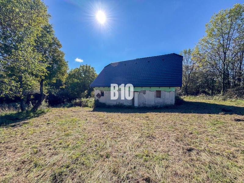 Chata v Lackově obklopená přírodou, s modrou střechou, slunečný den.