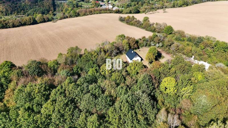 Chata v Lackově obklopená lesem a poli, klidná venkovská krajina.