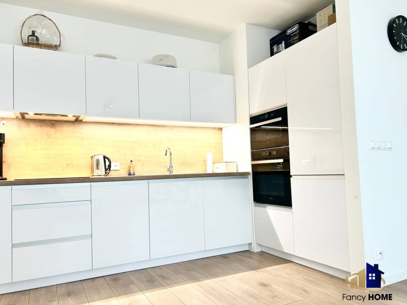 Kuchyně v 2-pokojovém bytě s bílými skříňkami a podlahou s dřevěným dekorem.