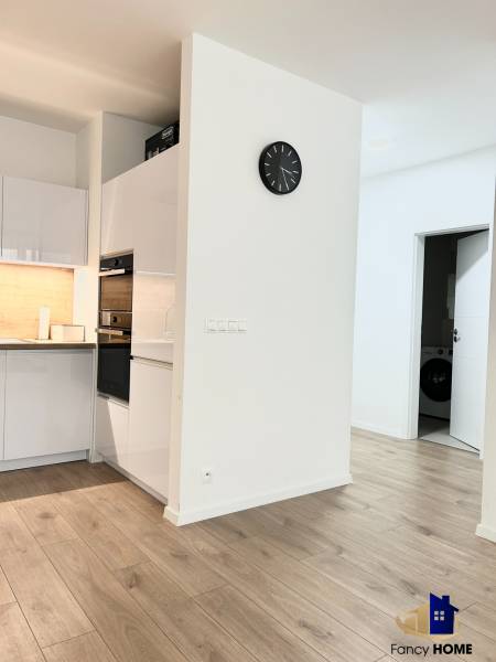 Kuchyně v 2-pokojovém bytě s dřevěným dekorem podlahy a bílým nábytkem.