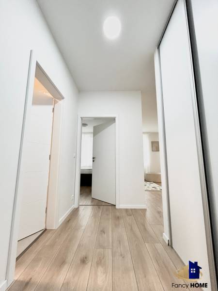 Chodba se světlými stěnami a podlahou s dřevěným dekorem, vedoucí do místností 2-pokojového bytu.