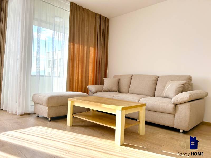 Obývací pokoj v dvoupokojovém bytě s pohovkou, stolkem a podlahou s dřevěným dekorem.