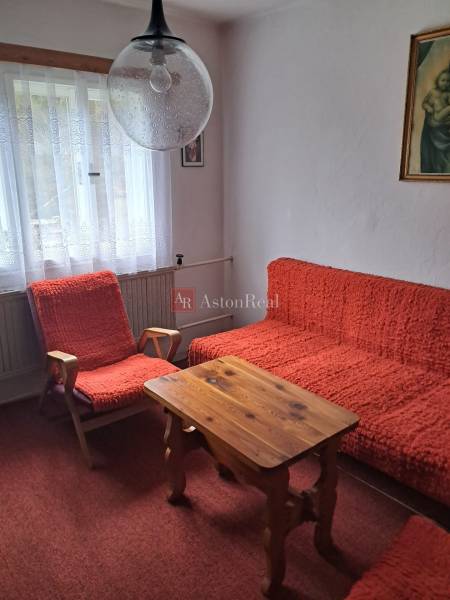 Pokoj v rodinném domě s červenými křesly, stolem a záclonovými závěsy.