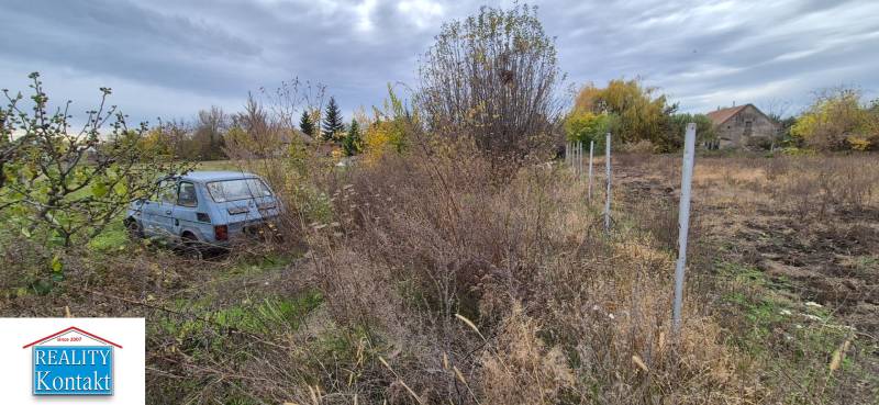 Pozemek na bydlení v Tvrdošovcích s opuštěným autem a zarostlým terénem.