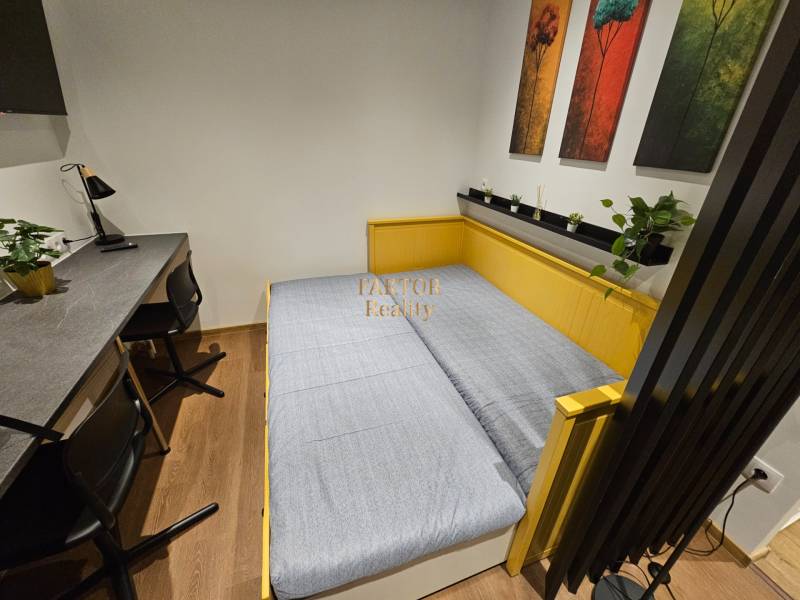 Garsonka s postelí, stolem, křesly a dekorativními obrazy, podlaha s dřevěným dekorem.