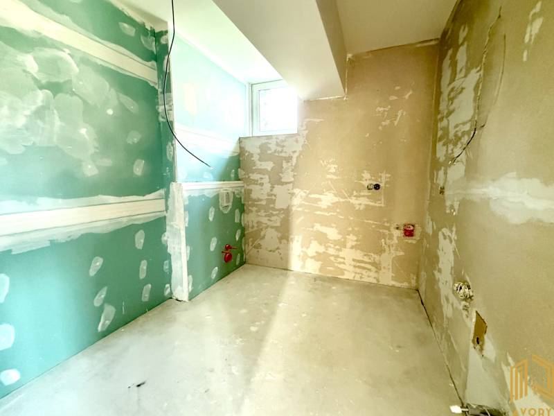 Je nedokončená místnost v 2-pokojovém bytě s holými stěnami a oknem.