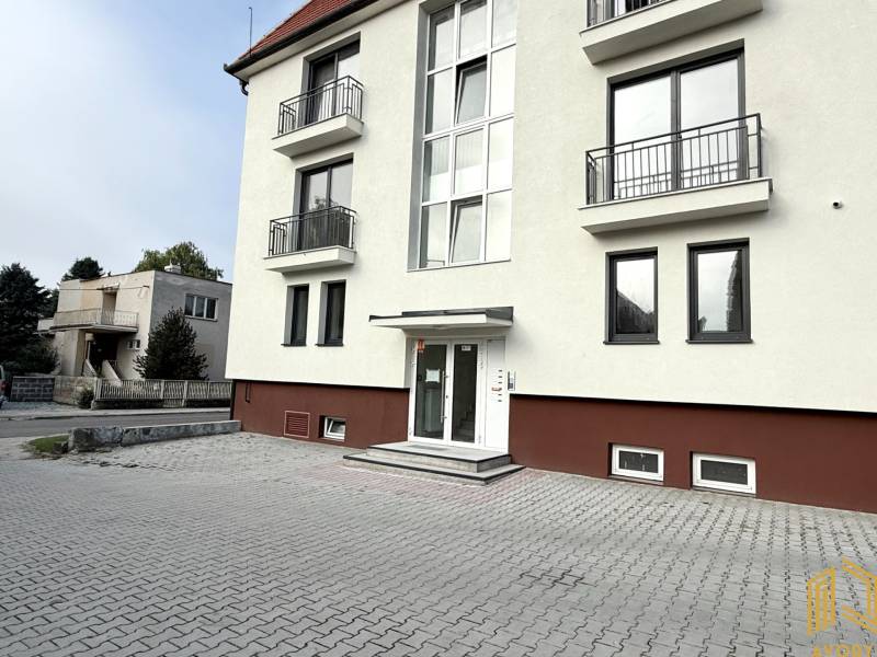 Budova na Sadové ulici v Senici s bílou fasádou a dlážděným parkovištěm.