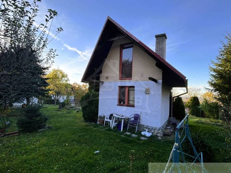 Chata v Sološnici s upravenou zahradou, obklopená stromy a jasnou oblohou.