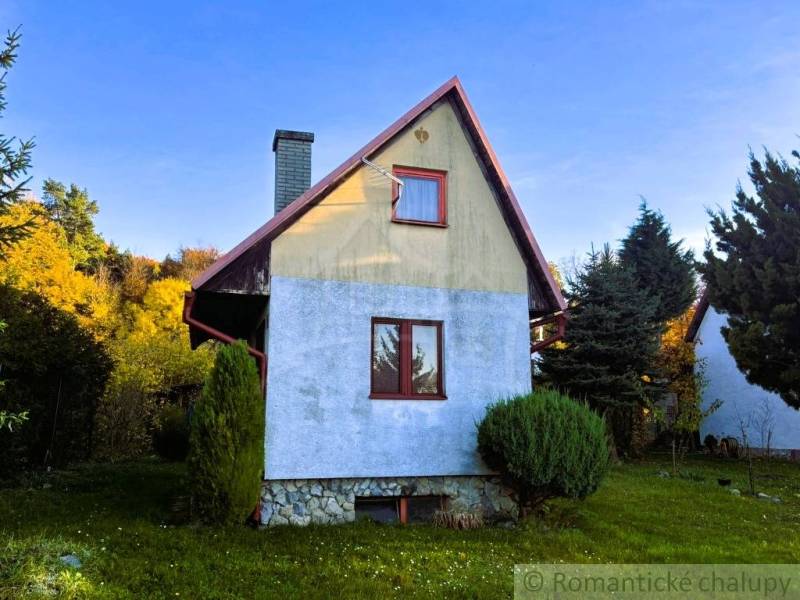 Chata v Sološnici obklopená zelení s modrou omítkou a šikmou střechou.