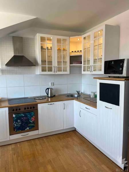 Kuchyně v 3-pokojovém bytě s dřevěnou podlahou, bílými skříňkami a úložným prostorem.