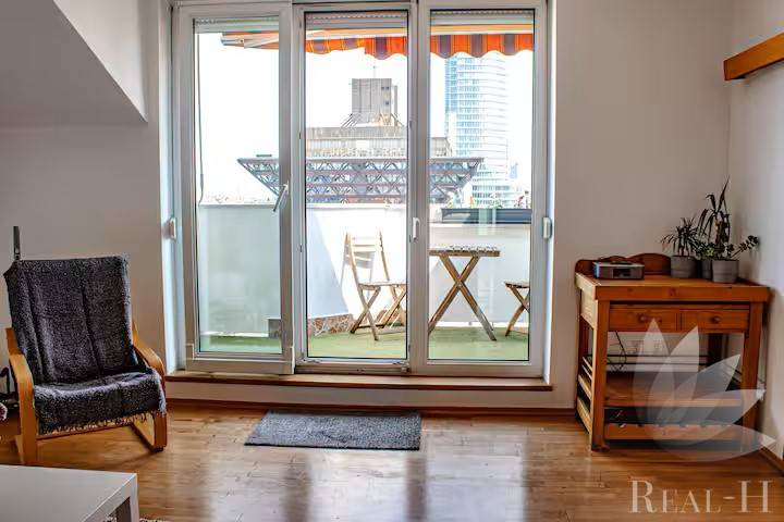 Obývací pokoj s balkonem, dřevěná podlaha, židle a stolek ve 3pokojovém bytě.