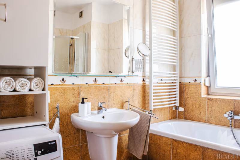 Koupelna v 3-pokojovém bytě s umyvadlem, vanou, pračkou a sušákem na ručníky.