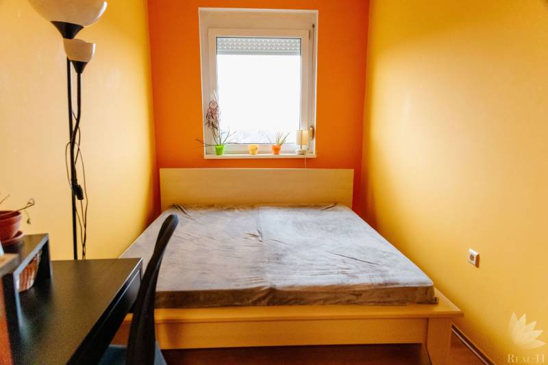 Ložnice s postelí, pracovním stolem a oknem ve dvoupokojovém bytě.