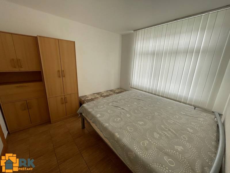 Ložnice v rodinném domě s bílými roletami, postelí a skříněmi.