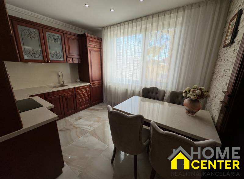 Kuchyně s tmavými skříňkami, bílými závěsy a květinovou dekorací v rodinném domě.