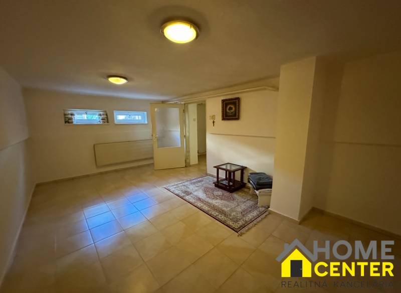 Interiér rodinného domu s dlažbou, kobercem, malými okny a jednoduchým stolkem.