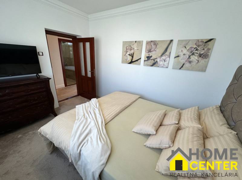 Ložnice rodinného domu s dekorativními obrazy na stěně, čalouněným nábytkem a dveřmi.