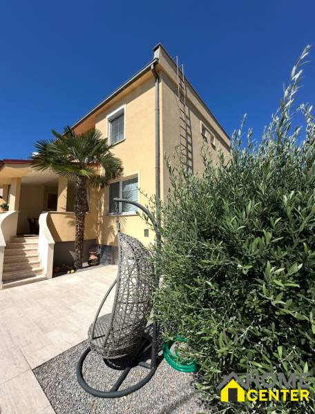 Rodinný dům v Komárně s terasou, zahradním křeslem a palmovým stromem na dvoře.