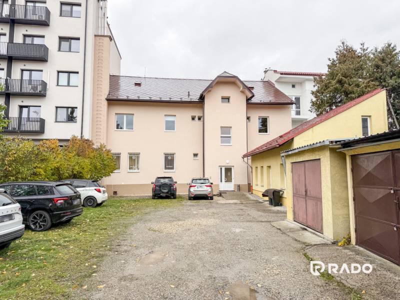 Budova na Bratislavské ulici v Žilině, obklopená auty a garážemi, vhodná pro kanceláře.