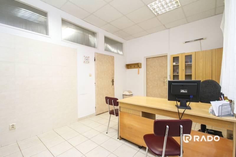 Kanceláře se stolem, židlí, počítačem a skříní na světlé keramické podlaze.