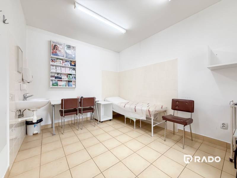 Místnost v kanceláři s dlažbou, umyvadlem, židlemi a lehátkem.