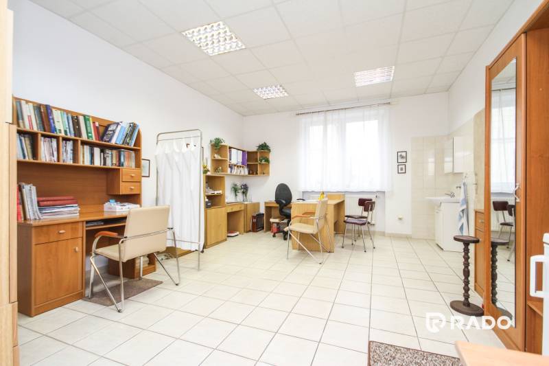 Kanceláře se stoly a židlemi, bílá keramická podlaha, police s knihami.