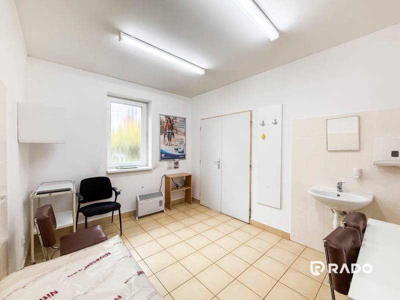 Ordinace s umyvadlem, židlemi a oknem s výhledem, podlaha se světlým dekorem.