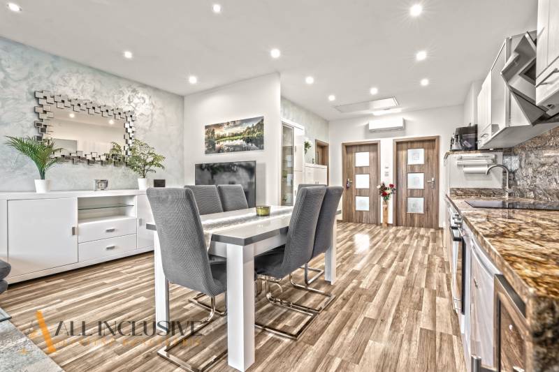 Jídelní kout ve 3-pokojovém bytě s podlahou s dřevěným dekorem a stylovým zrcadlem.