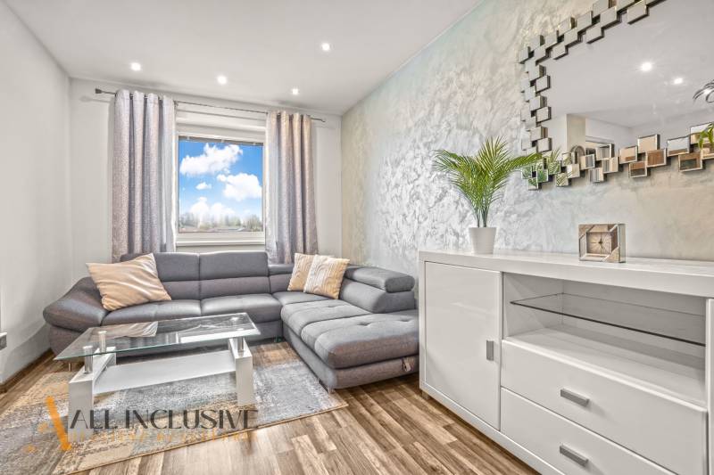 Obývací pokoj ve 3-pokojovém bytě s pohodlnou sedačkou a podlahou s dřevěným dekorem.