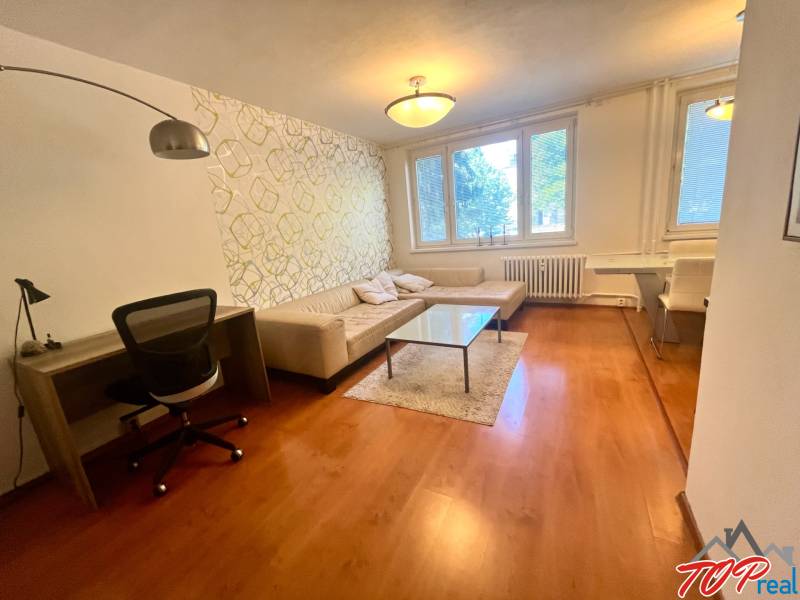 Obývací pokoj ve 3-pokojovém bytě s pohovkou, stolkem a pracovním stolem.