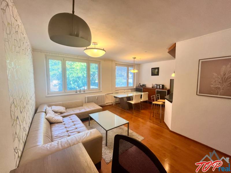 Obývací pokoj v 3-pokojovém bytě s pohovkou, stolem a jídelním koutem.