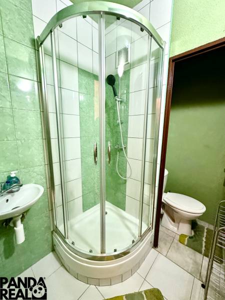 Koupelna v garsonce s rohovým sprchovým koutem, umyvadlem a bílými obkladačkami.