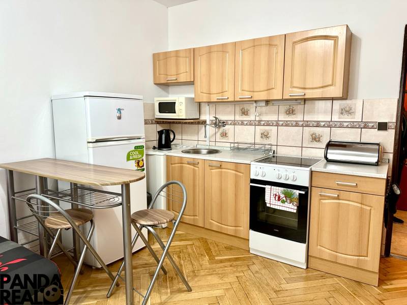 Kuchyně v garsonce s podlahou s dřevěným dekorem, se spotřebiči a sezením.