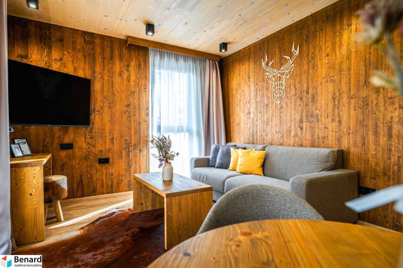 Obývací pokoj s dřevěnými stěnami, šedou pohovkou a podlahou s dřevěným dekorem v 2pokojovém bytě.