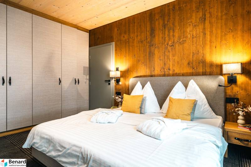 Ložnice v 2-pokojovém bytě s postelí, skříní a stěnou s dřevěným dekorem.