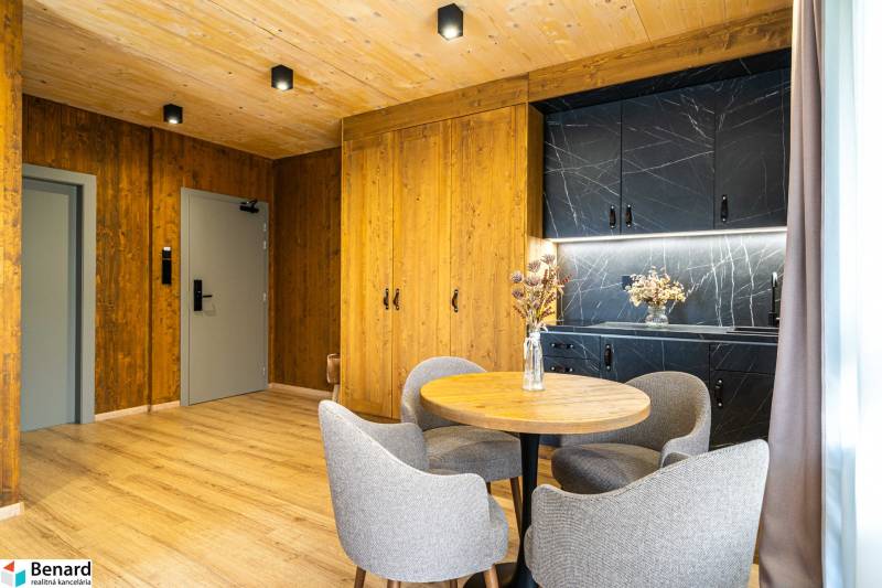 Interiér 2-pokojového bytu s podlahou s dřevěným dekorem, dřevěnými stěnami a černou kuchyňskou linkou.